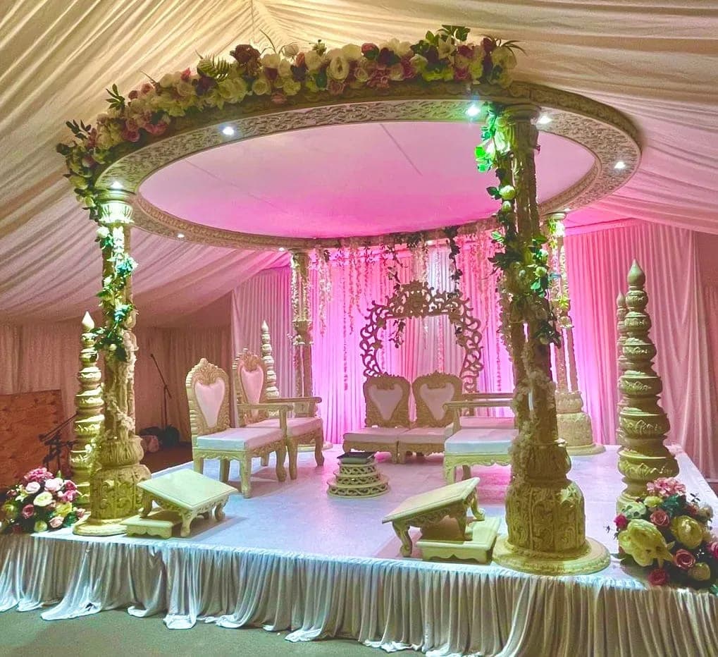 Oval carved mandap with pink lighting and heart-backed chairs on a draped platform inside a marquee Oval carved mandap with pink lighting and heart-backed chairs on a draped platform inside a marquee