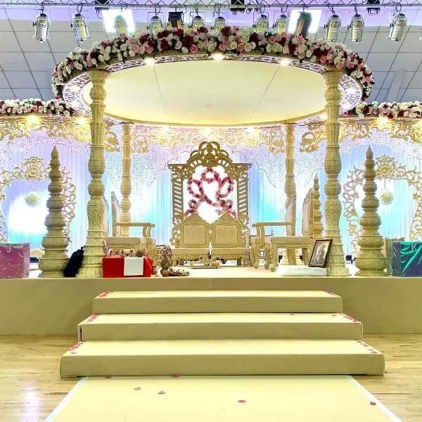 Cream and gold carved mandap with rose garland and throne backdrop on stage Cream and gold carved mandap with rose garland and throne backdrop on stage