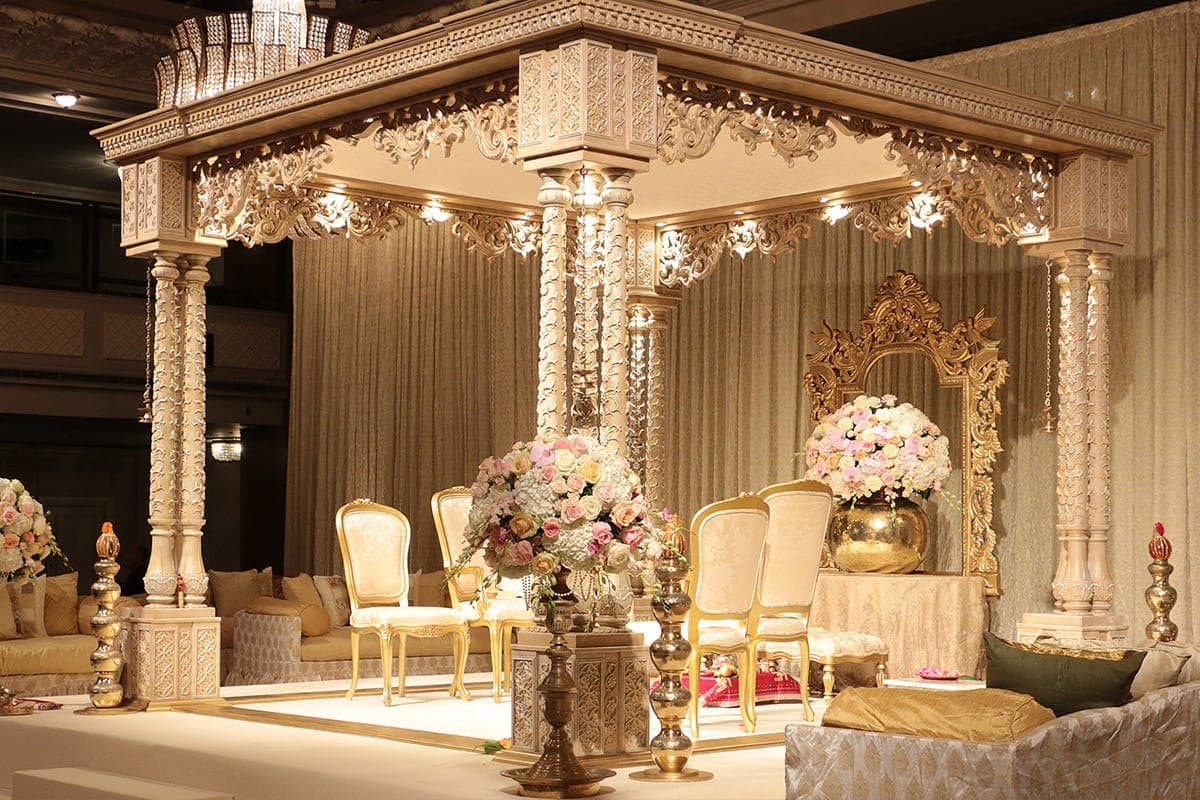 Carved cream four-pillar mandap with pink roses and gold chairs Carved cream four-pillar mandap with pink roses and gold chairs