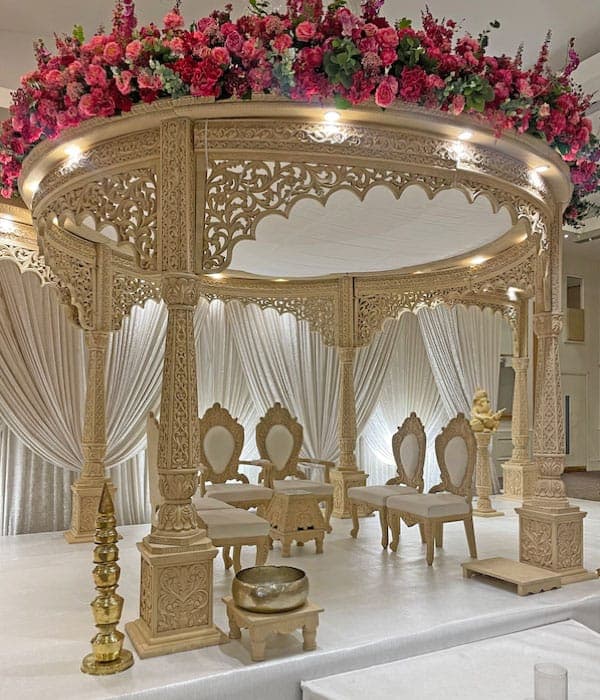 Pale carved oval mandap topped with deep pink roses and white drapes Pale carved oval mandap topped with deep pink roses and white drapes