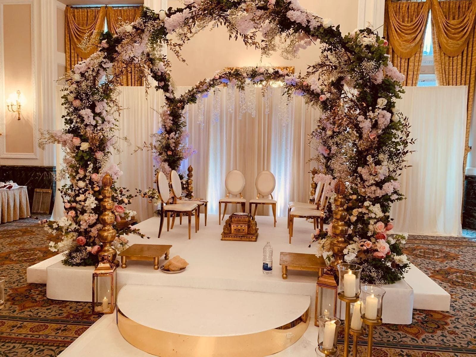 Double floral arch over a white stage with cream chairs and gold lanterns in a manor hall Double floral arch over a white stage with cream chairs and gold lanterns in a manor hall