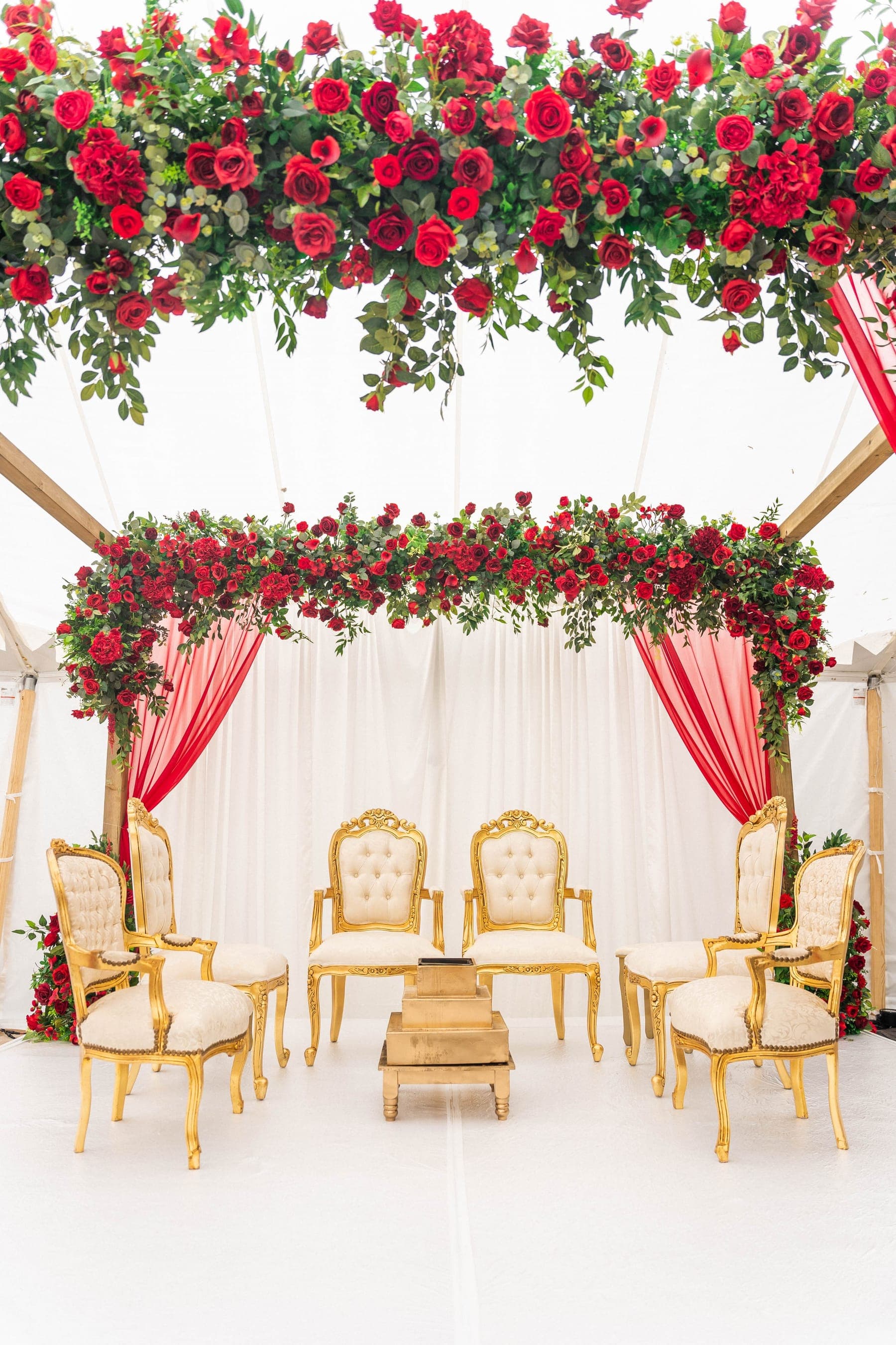 Red rose canopy over a timber frame with gold armchairs on a white platform Red rose canopy over a timber frame with gold armchairs on a white platform