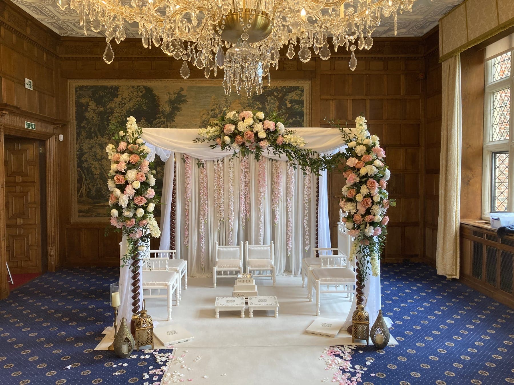 White drape frame with pastel floral posts under a chandelier on a navy patterned carpet White drape frame with pastel floral posts under a chandelier on a navy patterned carpet