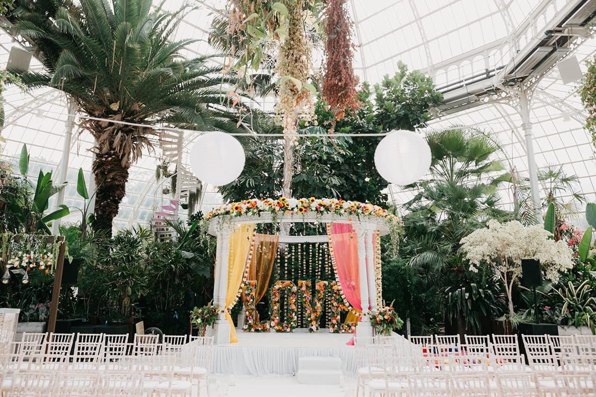 Glasshouse view of a white round mandap with sunflowers, saffron curtains and LOVE letters Glasshouse view of a white round mandap with sunflowers, saffron curtains and LOVE letters