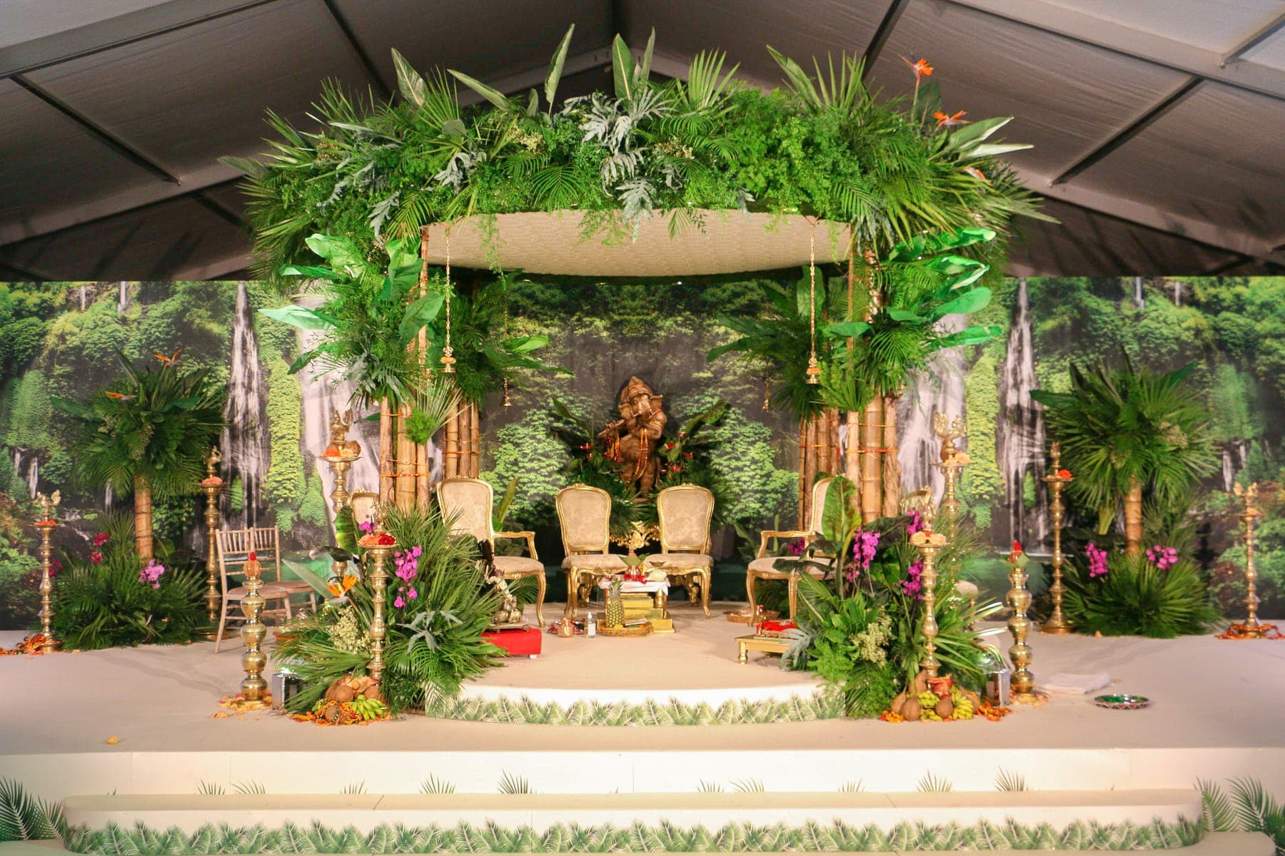 Tropical mandap with palms, orchids and bamboo posts before a waterfall backdrop Tropical mandap with palms, orchids and bamboo posts before a waterfall backdrop