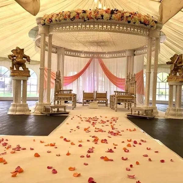 White lattice pillar mandap with peach garland and coral drapes, with orange petals along the runner White lattice pillar mandap with peach garland and coral drapes, with orange petals along the runner